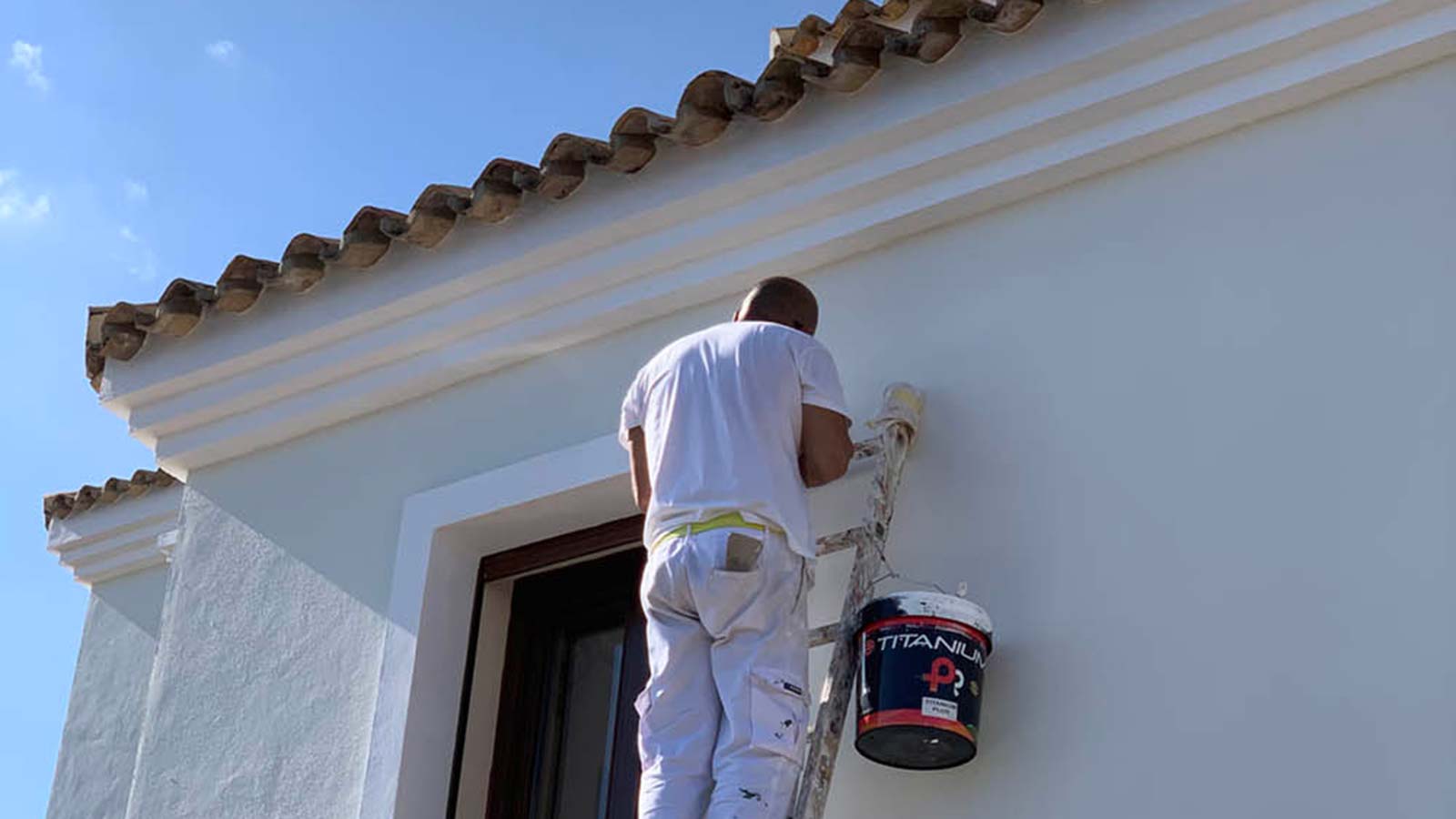 painter up a ladder painting an exterior wall of a spanish house